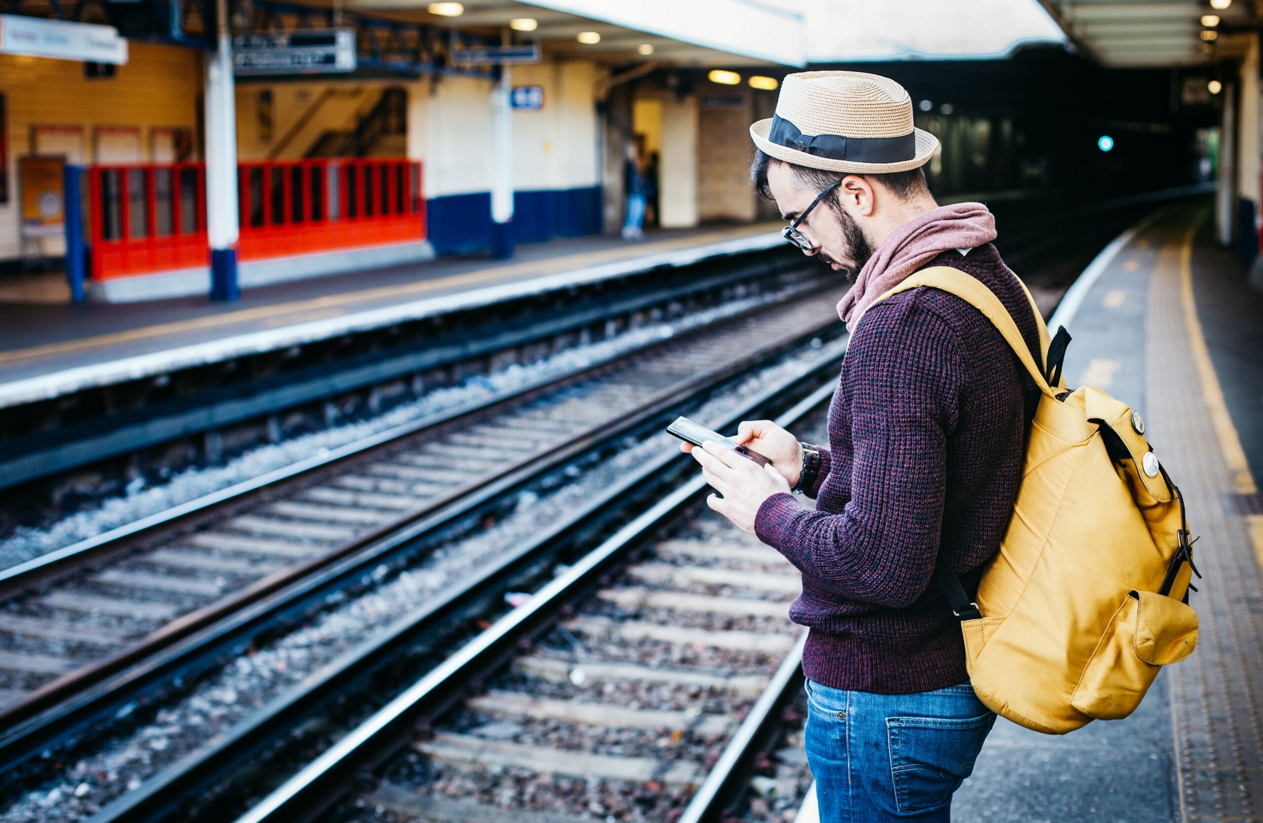 man using phone while standing in front of train rail during daytime